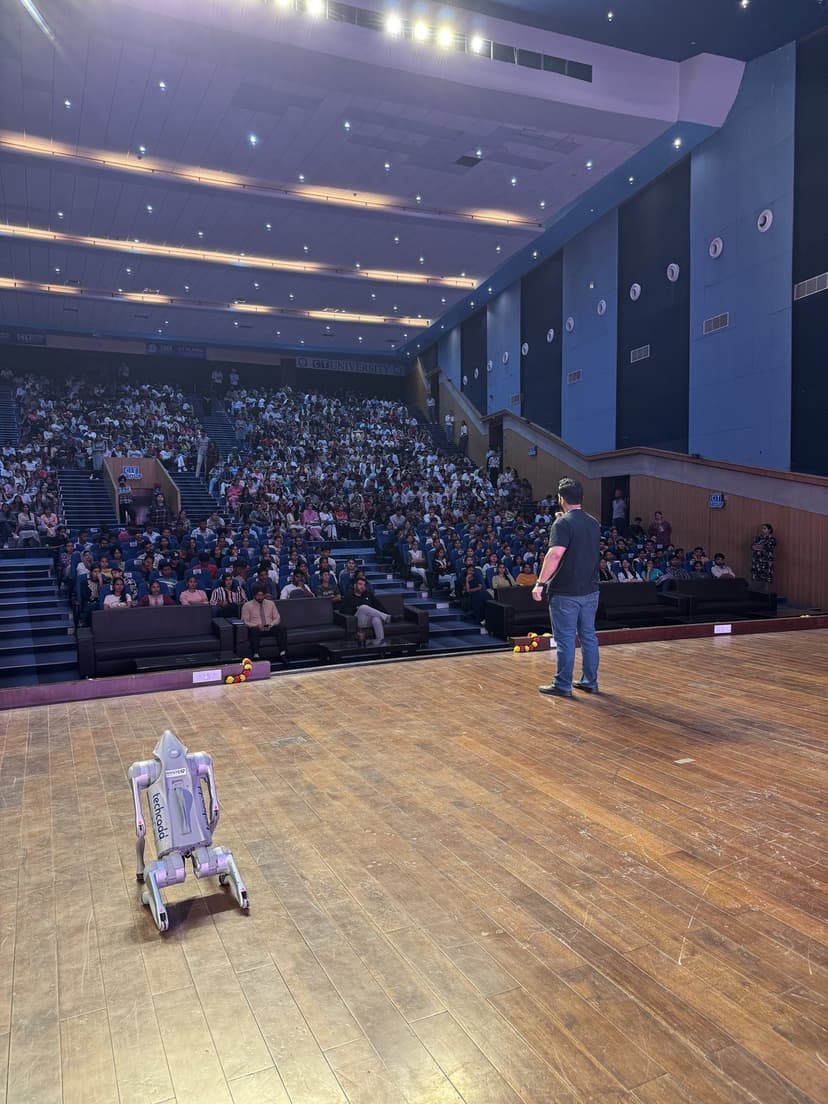 Gourav Gupta on stage in a large auditorium, with a robot on the stage floor beside him